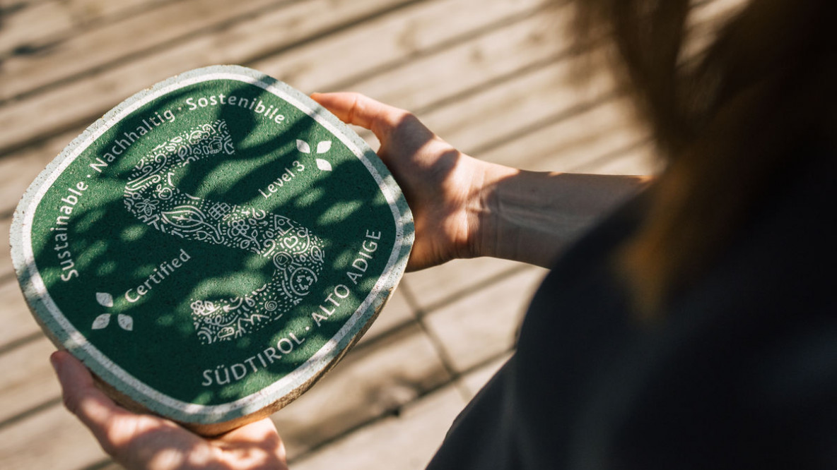 Eine Frau hält das grüne Schild des Nachhaltigkeitslabels Südtirol in den Händen.