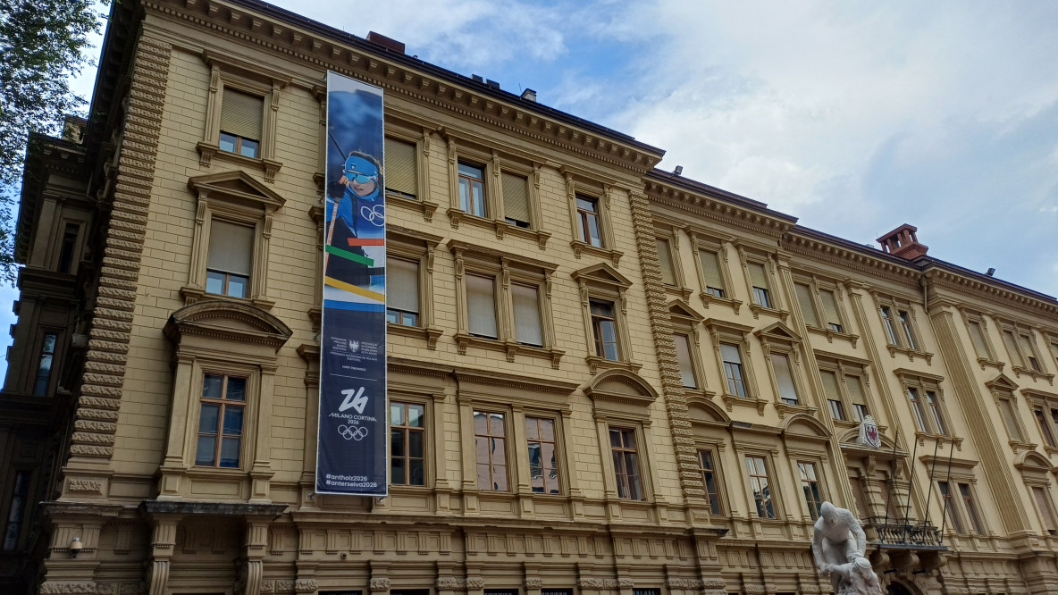 Il banner olimpico 2026 per Anterselva esposto su palazzo Widmann in piazza Silvius Magnago a Bolzano