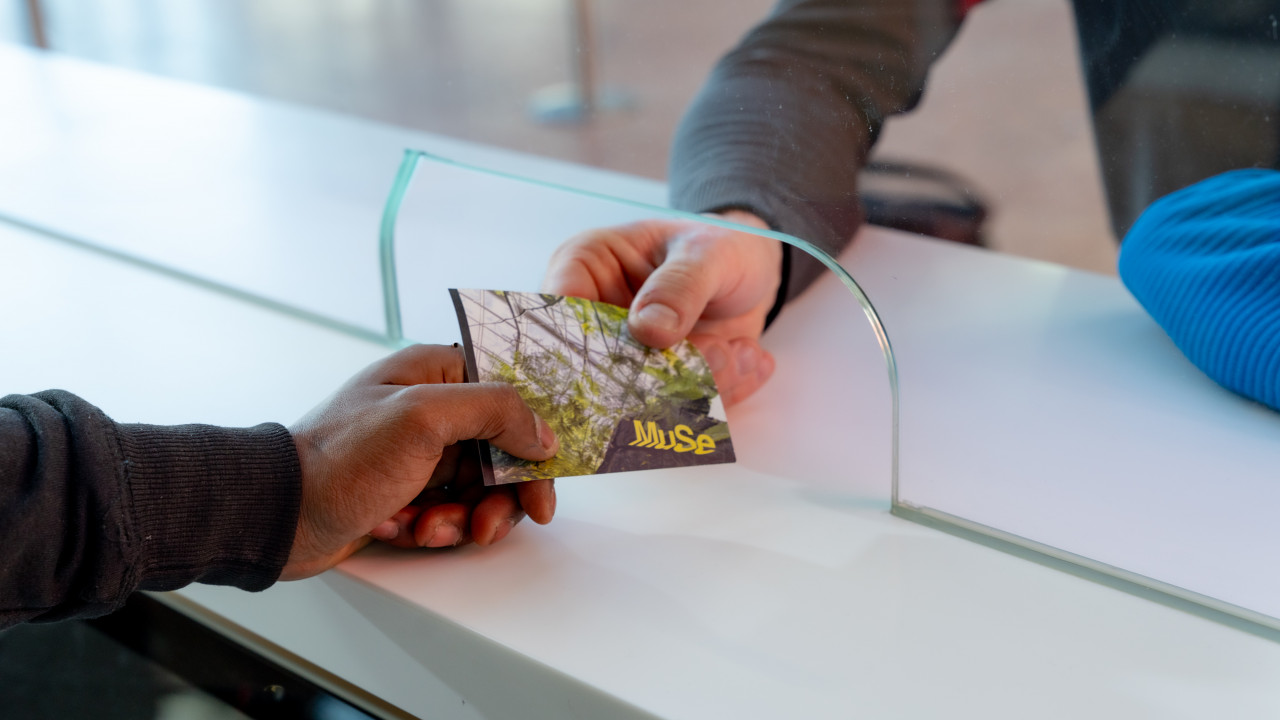 Eine Hand überreicht einer anderen Hand ein Ticket für das MUSE. 