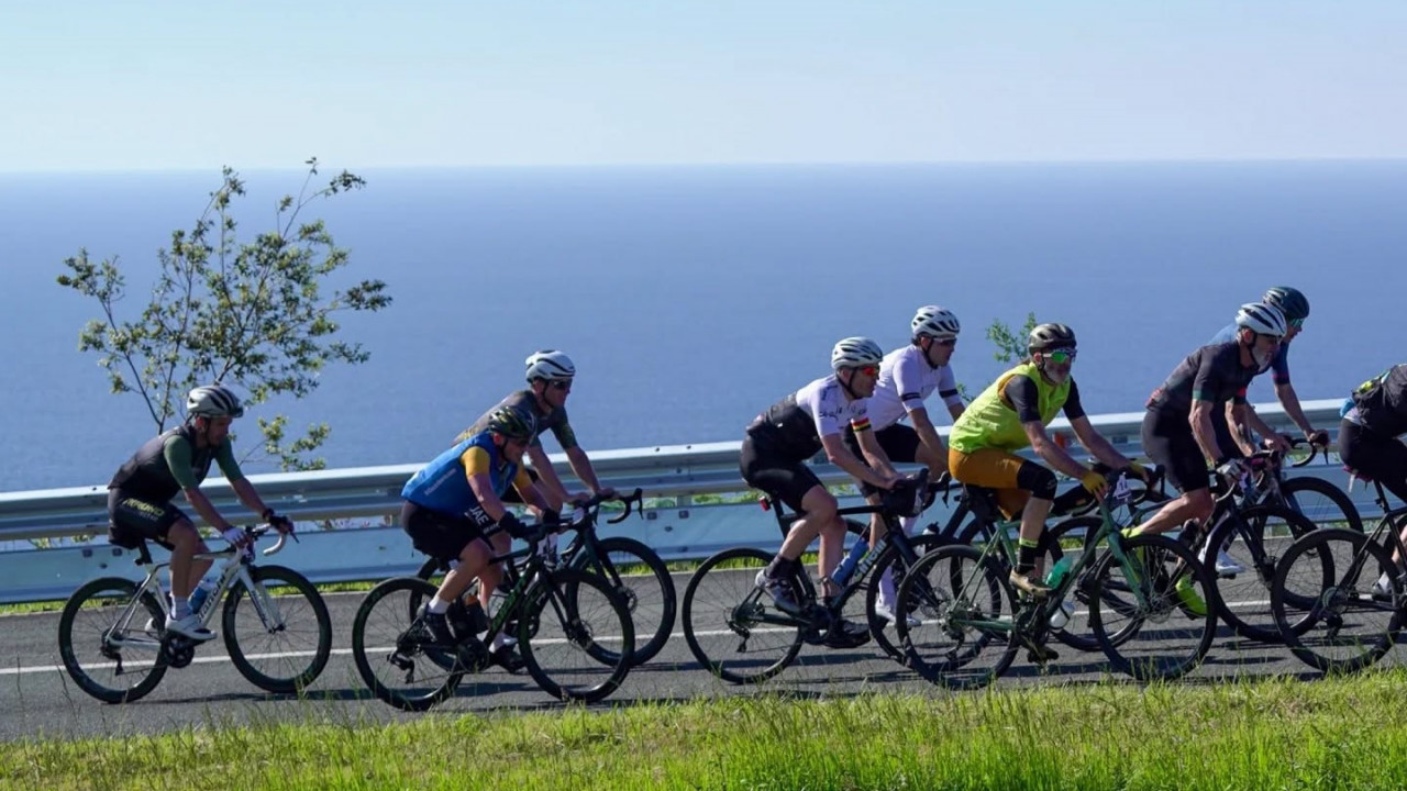Auf dem Bild sind mehrere Rennradfahrer, die am Meer entlang fahren.