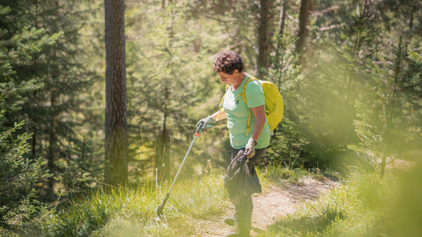 Donna che raccoglie rifiuti lungo un sentiero forestale durante un'attività di pulizia ambientale.