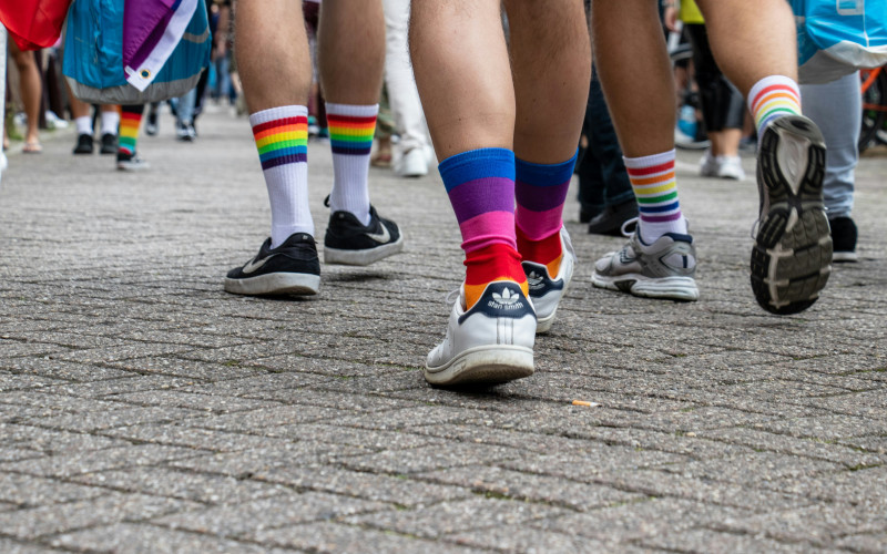 Auschnitt von mehreren Beinen in Turnschuhen und Regenbockensocken, die auf Straße gehen