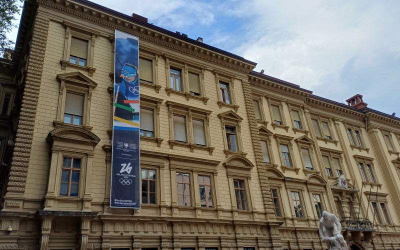 Il banner olimpico 2026 per Anterselva esposto su palazzo Widmann in piazza Silvius Magnago a Bolzano