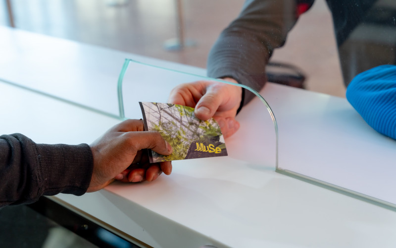 Eine Hand überreicht einer anderen Hand ein Ticket für das MUSE. 
